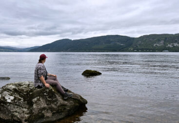 Ein Foto von mir auf einem Stein am Ufer des Loch Ness, wie ich auf das Wasser schaue