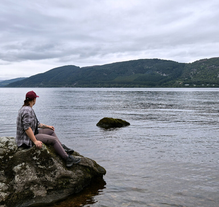Ein Foto von mir auf einem Stein am Ufer des Loch Ness, wie ich auf das Wasser schaue
